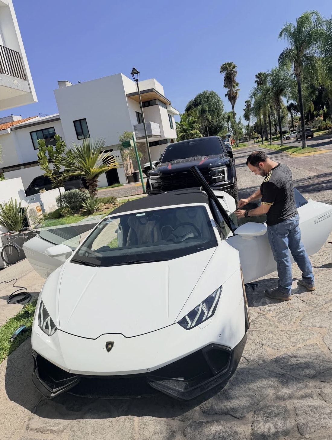 Instalador de Lalo's Cars colocando película en la puerta de un Lamborghini Huracán blanco, estacionado frente a la casa del cliente bajo el sol de Guadalajara