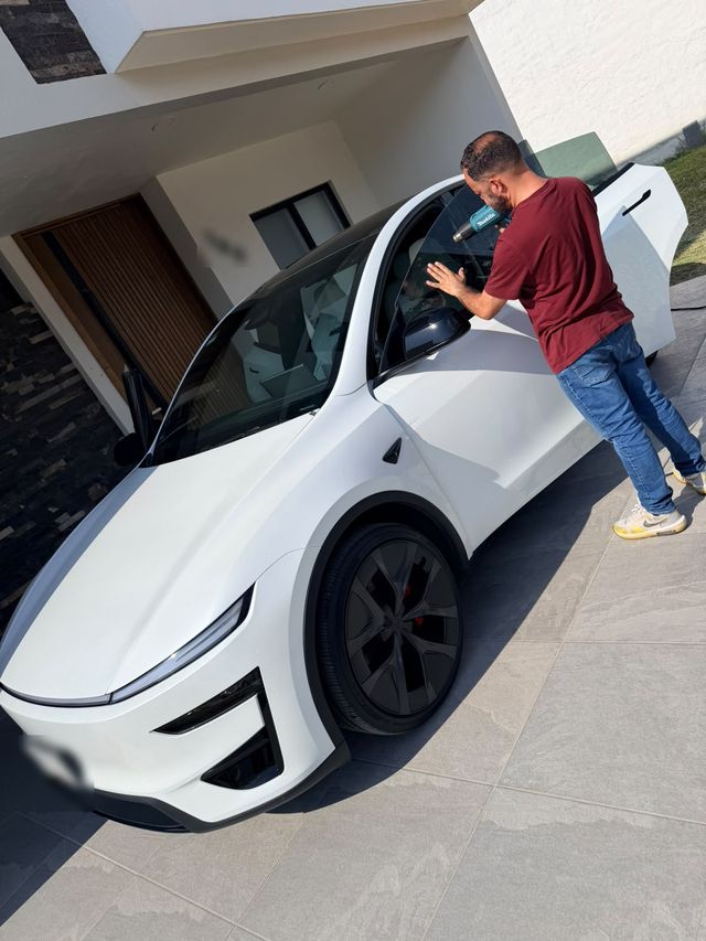 Instalador polarizando un Tesla Model Y blanco frente a la casa del cliente