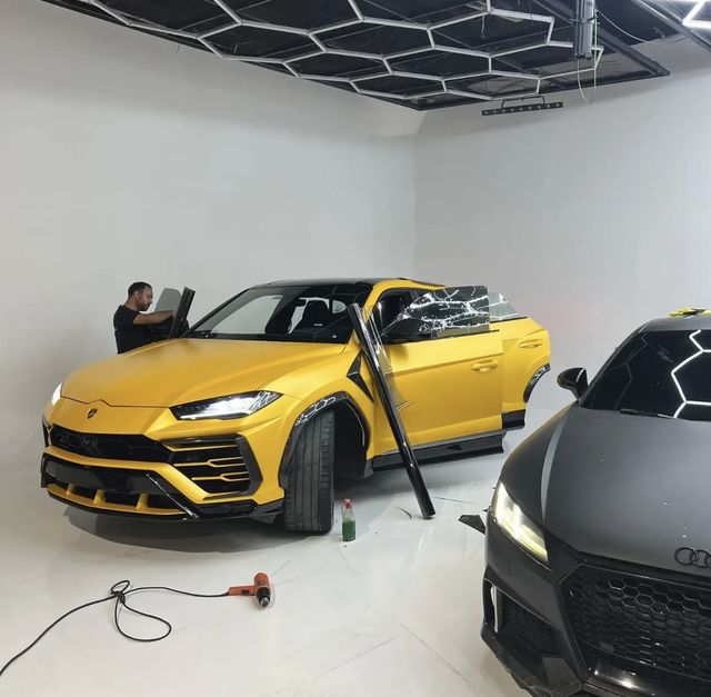 Instalador con un rollo de película junto a un Lamborghini Urus amarillo en un estudio